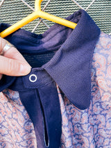 Women's or men's vintage 1970's long sleeve navy blue t-shirt with a paisley print on the front, a rounded dagger collar, and white popper buttons.