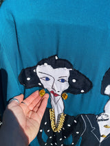 Women's vintage 1980's made in usa long sleeve blue blazer with one button closure and fully lined with large patches of people on front and back.