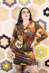 Women's vintage 1970's long sleeve knee length dress in a polyester material with a tie front neck. Brown color with all over yellow and orange flowers.