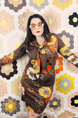 Women's vintage 1970's long sleeve knee length dress in a polyester material with a tie front neck. Brown color with all over yellow and orange flowers.