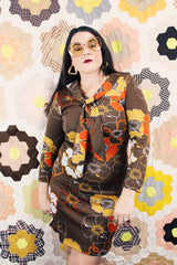 Women's vintage 1970's long sleeve knee length dress in a polyester material with a tie front neck. Brown color with all over yellow and orange flowers.