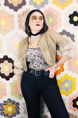 Women's vintage 1970's cropped fit tan suede jacket with short sleeves and two snap button closure in the front. Sleeves have a cream fur trim.