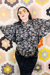 Women's vintage 1970's lightweight polyester material black blouse with all over multicolored ditsy floral print. Buttons up the front and has big wing sleeves.