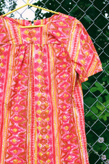 Women's vintage 1970's short sleeve midi length smock house dress in a pink, yellow, and light brown abstract print.