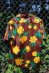 Men's vintage 1980's Hilo Hatties Hawaii label short sleeve button up floral print Hawaiian shirt in silky polyester material. Brown with all over yellow flowers.