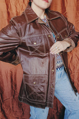 Women's or men 's vintage 1970's Montgomery Ward label long sleeve chocolate brown colored leather jacket with contrast stitching and popper buttons.