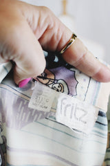 Women's vinttage 1970's Fritz label short sleeve button up blouse with dagger collar and all white, blue, and purple novelty print in a lightweight polyester material.