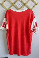 Women's or men's vintage 1980's short sleeve red tee with white trim around v shaped neckline. White sleeves have red stripes. White graphic on left chest.