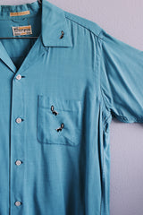 Men's vintage 1950's Skipper, Wilson Brothers, Made in USA, Custom Detailed label short sleeve blue button up shirt in cotton material with small embroidered skunks.