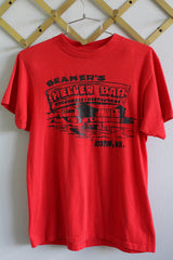 Women's or men's vintage 1980's short sleeve red colored t-shirt with a big black graphic on the front and back with text. Ribbed collar, medium size.