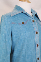 Women's vintage 1970's long sleeve medium wash denim chambray button up blouse with red contrast stitching and brass buttons.
