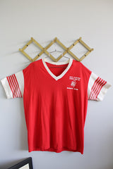 Women's or men's vintage 1980's short sleeve red tee with white trim around v shaped neckline. White sleeves have red stripes. White graphic on left chest.