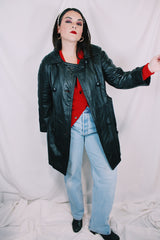 Women's vintage 1970's long sleeve double breasted long length black leather jacket with fabric buttons and side pockets. Matching belt.
