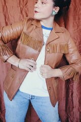 Women's vintage 1950's Custom Made by Milco-West, Portland, Oregon label long sleeve button up tan camel colored leather jacket with fringe trim. Western style with four pockets.