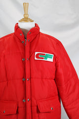 Women's or men's vintage 1980's Tonkin Wearables, Woodinville, WA, Made in USA label long sleeve bright red nylon puffer jacker with patch on left chest and a zipper and popper buttons closure.
