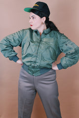 Men's vintage 1980's Flyer's CWU Military Flyer's Jacket, Made in USA label size medium long sleeve cropped length army green zip up bomber jacket with orange liner.
