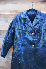Women's vintage 1960's long sleeve black vinyl material jacket with gold buttons and hardware. Fully lined and has two side pockets.