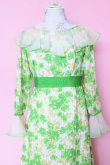 Women's vintage 1970's long sleeve maxi length floral print dress in green and white colors. Sheer white ruffle trim, ribbon belt.