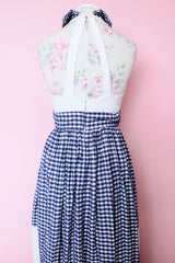 Women's vintage 1970's sleeveless halter neck maxi style halter dress in white and navy gingham print with red bowtie at neck and two front pockets on skirt with flowers.