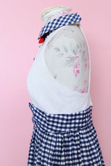 Women's vintage 1970's sleeveless halter neck maxi style halter dress in white and navy gingham print with red bowtie at neck and two front pockets on skirt with flowers.