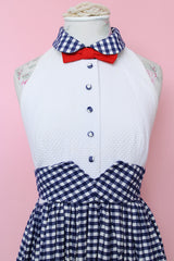 Women's vintage 1970's sleeveless halter neck maxi style halter dress in white and navy gingham print with red bowtie at neck and two front pockets on skirt with flowers.
