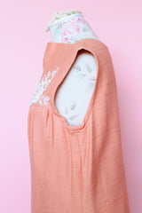 Women's vintage 1960's midi length sleeveless peach orange colored shirt dress with white beads across chest creating a floral print.