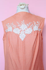 Women's vintage 1960's midi length sleeveless peach orange colored shirt dress with white beads across chest creating a floral print.