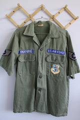 Men's vintage 1960's Guaranteed Trooper Fatigues label short sleeve army green button up shirt or jacket with US Air Force patches all over.