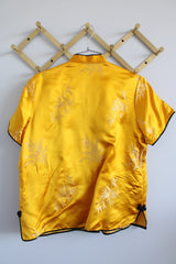 Women's vintage 1960's short sleeve gold yellow stain button up blouse with black trim and black fabric buttons.