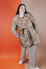 Women's vintage 1960's long sleeve knee length faux fur tan coat with leather trim. Has a matching leather belt, gold twist buttons, and pockets