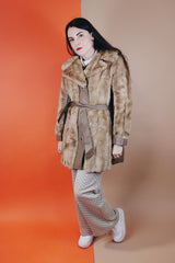 Women's vintage 1960's long sleeve knee length faux fur tan coat with leather trim. Has a matching leather belt, gold twist buttons, and pockets