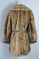 Women's vintage 1960's long sleeve knee length faux fur tan coat with leather trim. Has a matching leather belt, gold twist buttons, and pockets