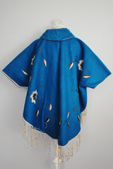 blue wool poncho with white embroidered flowers and white fringe on hem vintage