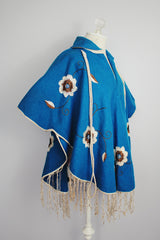 blue wool poncho with white embroidered flowers and white fringe on hem vintage