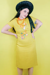 Women's vintage 1960's Jan Sue label short sleeve knee length shift dress in yellow cotton with multicolored floral print stitched on the front.