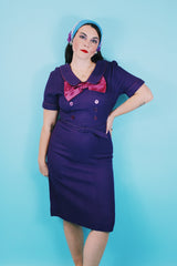 Women's vintage 1960's Mode O'Day label short sleeve knee length purple wool blend dress with peter pan collar, satin bow, matching belt, and decorative buttons.