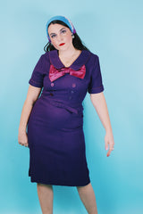 Women's vintage 1960's Mode O'Day label short sleeve knee length purple wool blend dress with peter pan collar, satin bow, matching belt, and decorative buttons.