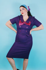 Women's vintage 1960's Mode O'Day label short sleeve knee length purple wool blend dress with peter pan collar, satin bow, matching belt, and decorative buttons.