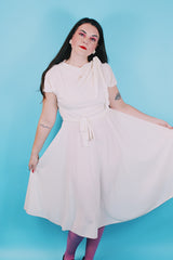 Women's vintage 1970's short sleeve capped sleeved midi length off white cream dress with draped neckline, attached tie bow on shoulder, elastic waistband, and detachable matching tie belt