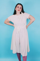 Women's vintage 1970's short sleeve capped sleeved midi length off white cream dress with draped neckline, attached tie bow on shoulder, elastic waistband, and detachable matching tie belt