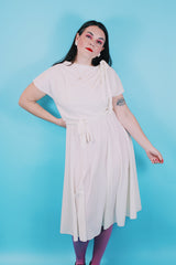 Women's vintage 1970's short sleeve capped sleeved midi length off white cream dress with draped neckline, attached tie bow on shoulder, elastic waistband, and detachable matching tie belt