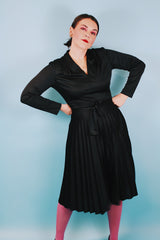 Women's vintage 1970's Joan Curtis long sleeve midi length black dress with pleated accordion skirt, a V shaped neckline, and detachable matching tie belt.