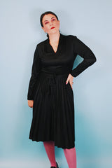 Women's vintage 1970's Joan Curtis long sleeve midi length black dress with pleated accordion skirt, a V shaped neckline, and detachable matching tie belt.