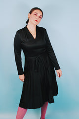 Women's vintage 1970's Joan Curtis long sleeve midi length black dress with pleated accordion skirt, a V shaped neckline, and detachable matching tie belt.