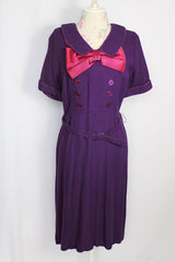 Women's vintage 1960's Mode O'Day label short sleeve knee length purple wool blend dress with peter pan collar, satin bow, matching belt, and decorative buttons.