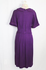 Women's vintage 1960's Mode O'Day label short sleeve knee length purple wool blend dress with peter pan collar, satin bow, matching belt, and decorative buttons.