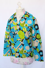 Women's vintage 1970's long sleeve collared blouse with zipper in the back and V shaped neckline. Polyester material in green and blue all over print.