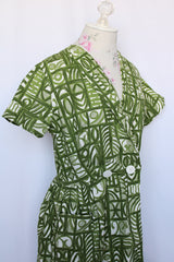 Women's vintage 1960's short sleeve midi length green and white printed wrap dress with two big white buttons at waist.