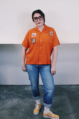 Men's vintage 1960's Joel's Striker short sleeve orange button up bowling shirt with three patches sewn on. Rayon acrylic blend material. One chest pocket and small collar.