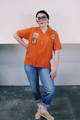 Men's vintage 1960's Joel's Striker short sleeve orange button up bowling shirt with three patches sewn on. Rayon acrylic blend material. One chest pocket and small collar.
